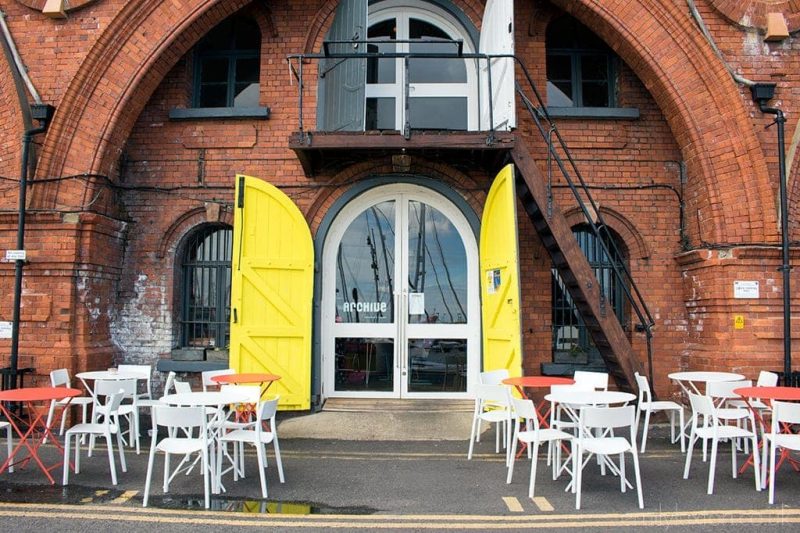 Red brick arch with glass doors in the centre and cafe tables outside