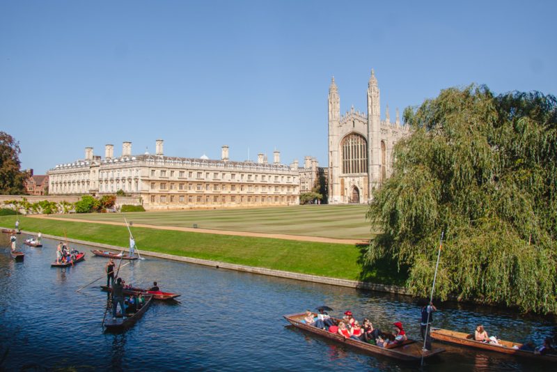 Several small wooden punting boats on the river in Cambridge with a large cathedral behind on a sunny day with clear blue sky