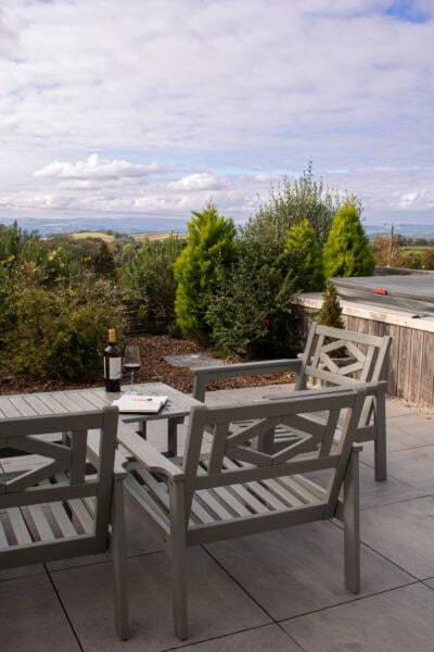 Bottle and glass of red wine on a wooden table on a patio with trees and views of countryside beyond