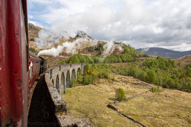 Looking out the window of a steam train as it crosses a stone viaduct
