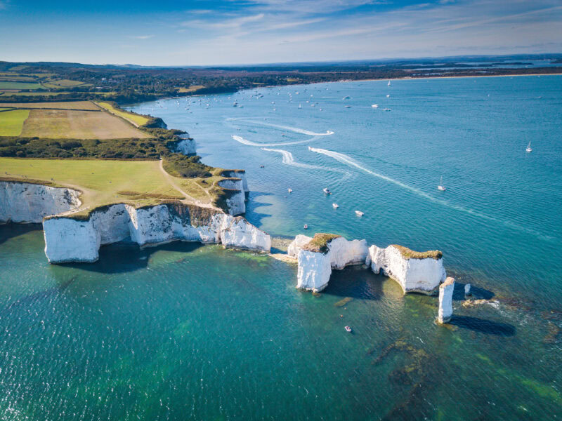 Aerial view of Old Harry Rocks with a series of tall white chalk rock stacks extending into the sea from a grassy headland near Swanage