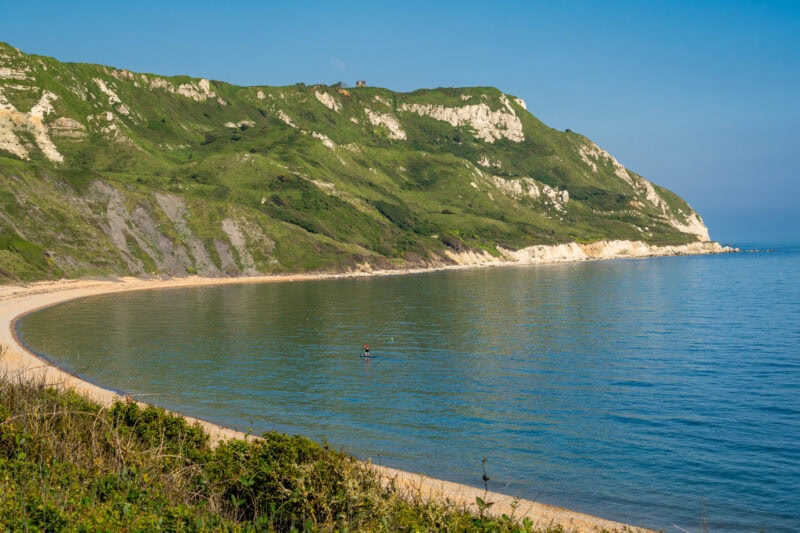 a shingle beach in a small bay towards a grassy headland 
