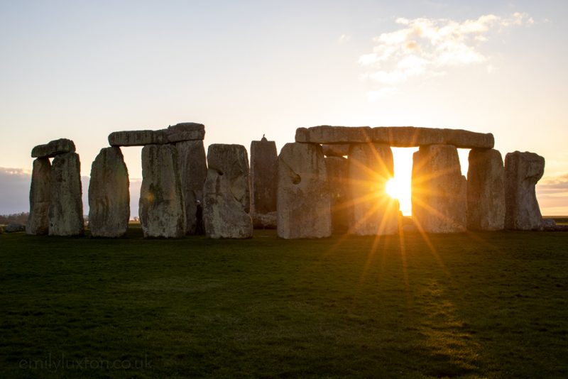 Stonehenge at sunset, a circle of standing stones with the setting sun flaring through one of the arches