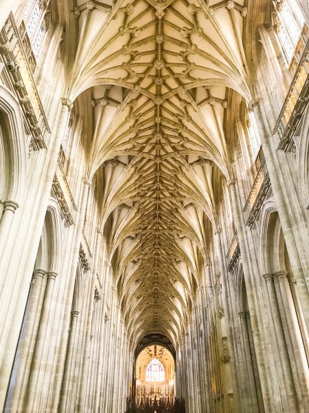 Winchester cathedral interior, looking up at the vaulted cieling with a stained glass window just visible at the far end