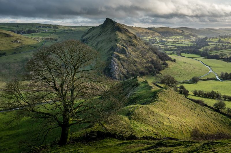 small conical hill with rocks on surrounded by green countyside in the peak district